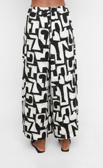 Load image into Gallery viewer, Back bottom half view of a woman wearing the ozai n ku puzzle letterpress palazzo pants
