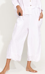Load image into Gallery viewer, Front bottom half view of a woman wearing the banana blue solid white pant. This pant has two front pockets and a wide cropped cut.
