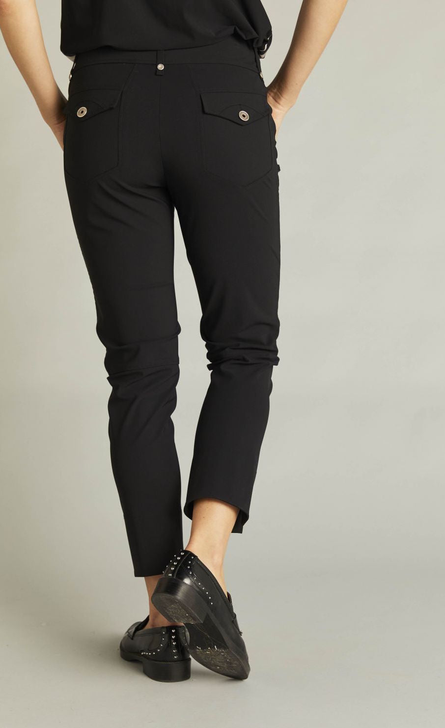 Back bottom half view of a woman wearing the black indies epatant pants. These pants have two flap back pockets.