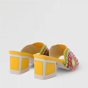 Back view of a pair of the kat maconie vira kicker heel sandals. These mule sandals are mineral yellow with multi colored flowers on the sides. These sandals also have a block heel and an open toe front.