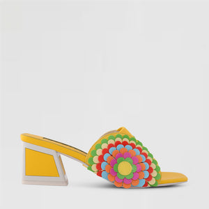 Outer side view of the kat maconie vira kicker heel sandals. These mule sandals are mineral yellow with multi colored flowers on the sides. These sandals also have a block heel and an open toe front.