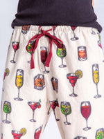 Load image into Gallery viewer, Close up view of a woman wearing the pj salvage call me old fashioned flannel pj set. The model has on an ivory colored long pant with cocktail glasses all over it and a wine colored drawstring waistband.
