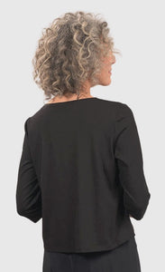 Back top half view of a woman wearing black pants and the alembika tekbika dune crop jacket. The back of this jacket is solid black. The jacket also has 3/4 length sleeves.