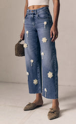 Load image into Gallery viewer, Person wearing blue jeans with floral patches on a neutral background
