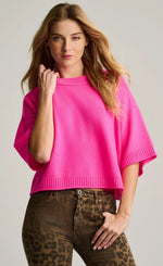 Load image into Gallery viewer, A woman wearing a bright pink knit short-sleeve top with a crew neck and wide sleeves, paired with brown leopard-print pants, against a light gray studio background.
