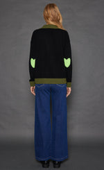 Load image into Gallery viewer, Back full body view of a woman wearing the lisa todd polo pop in onyx with green trim light green hearts on the elbows.
