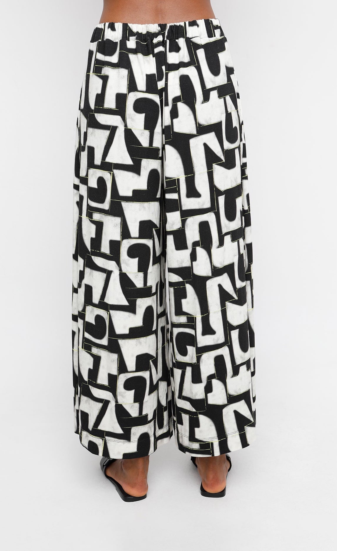 Back bottom half view of a woman wearing the ozai n ku puzzle letterpress palazzo pants