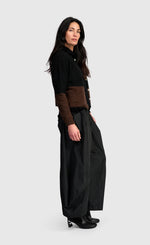 Load image into Gallery viewer, A woman modeling a black knit cardigan with brown color-blocked sleeves and waist detail, paired with black wide-leg trousers and black ankle boots, against a light gray studio background.

