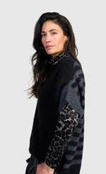 Load image into Gallery viewer, A woman modeling a black knit sweater with gray striped sleeves and leopard-print elbow patches, photographed against a light gray studio background.
