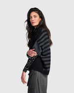 Load image into Gallery viewer, A woman modeling a dark gray and black striped knit sweater with leopard-print sleeves, paired with gray trousers, against a solid light gray background.
