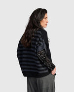Load image into Gallery viewer, A woman shown from the back wearing a black and dark gray striped knit cardigan with leopard-print elbow patches, paired with gray trousers, against a light gray studio background.
