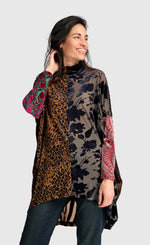 Load image into Gallery viewer, A woman modeling a long-sleeve tunic top with a mixed print design featuring leopard print, floral pattern, and red paisley sleeves, paired with dark jeans against a light gray background.
