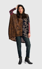 Load image into Gallery viewer, A woman modeling a long-sleeve, high-neck patchwork poncho top with leopard print, floral print, and red patterned sleeves, paired with dark jeans and black ankle boots, against a light gray background.
