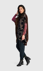 Load image into Gallery viewer, A woman modeling a long, open-front tunic-style cardigan with a dark brown and black abstract pattern, featuring bright pink and red patterned sleeves, paired with dark jeans and black ankle boots against a light gray background.
