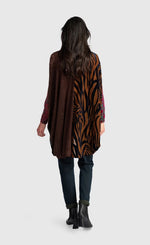 Load image into Gallery viewer, A woman shown from the back wearing a long-sleeve tunic top with a split design: one side is dark brown textured fabric and the other side features a brown and black tiger-stripe pattern. She is also wearing dark blue jeans and black ankle boots against a light gray studio background.
