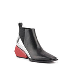 Load image into Gallery viewer, A black leather ankle boot with a geometric wedge heel, featuring a metallic silver side panel and a bright red heel block, shown against a plain white background.
