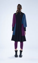 Load image into Gallery viewer, Back full body view of a woman wearing the luukaa color block tunic/dress. This knee-length dress is black with a blue and purple color blocking on the sides and sleeves. The dress also has elbow-length sleeves and a funnel neck.
