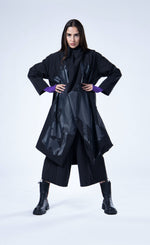 Load image into Gallery viewer, Front full body view of a woman wearing the luukaa draped open black coat. This coat is black with a black contrast, glossy abstract print on the front. The coat has long sleeves, a billowy fit, and a draped open front with a hem that sits at the knees.
