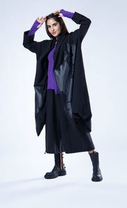 Front full body view of a woman wearing the luukaa draped open black coat. This coat is black with a black contrast, glossy abstract print on the front. The coat has long sleeves, a billowy fit, and a draped open front with a hem that sits at the knees.