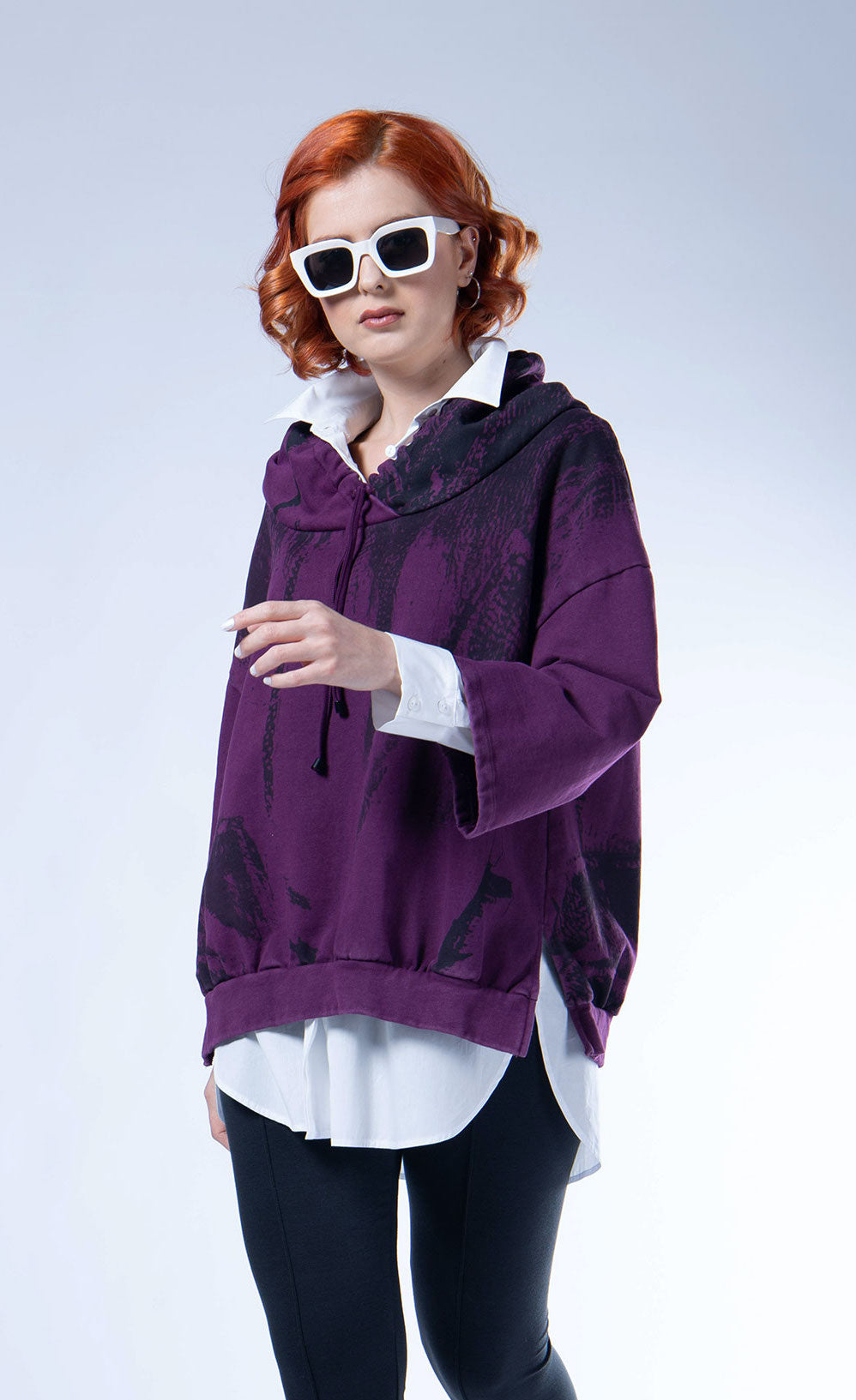 Front top half view of a woman wearing the luukaa aubergine sweatshirt with a faded black print. This sweatshirt has an oversized fit, drop shoulders, and 3/4 length sleeves. The sweatshirt also has a hood and a ribbed hem.