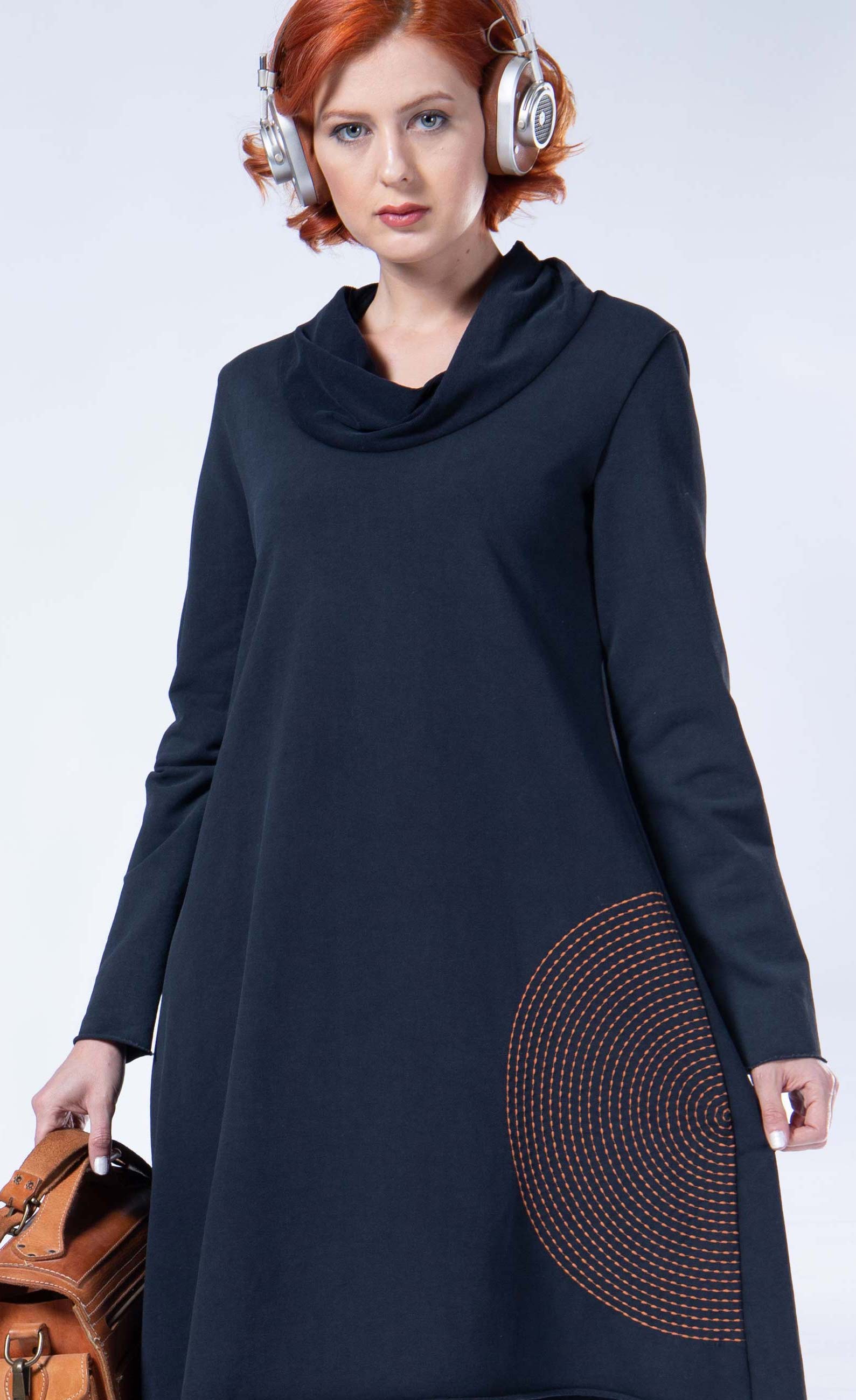 front top half view of a woman wearing the luukaa circles tunic/dress. This dress is black with an orange half-circle in the bottom left hand corner. The dress has long sleeves, a cowl neck, and sits at the knees.