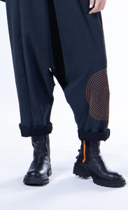 front bottom half view of a woman wearing the luukaa sleeveless circles jumper. This jumper is black with orange stitched circles all over it. The jumper has long pants with a crop crotch.
