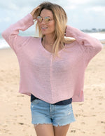 Load image into Gallery viewer, Front top half view of a woman on the beach wearing the wooden ships maui v cotton sweater in pink conch. This top has extra long sleeves, a v-neck, and a loose knit.
