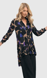 Front top half view of a woman wearing the alembika amethyst crinkle tunic blouse. This tunic is tan with black, purple, and blue large animal print on it. The top has a button down front, a collar, crinkle fabric, and long sleeves.