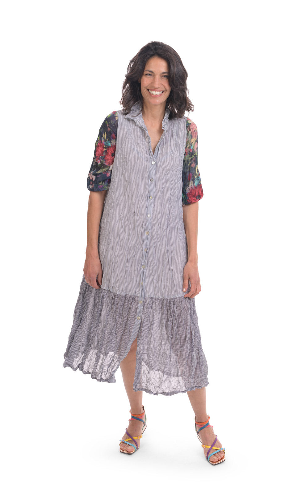 Front full body view of a woman wearing the alembika flora dress. This dress has navy and white striping, a button down front, and floral 3/4 sleeves. The bottom 1/4 of the dress is more transparent than the top 3/4.