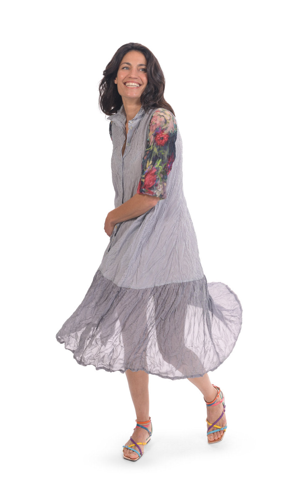 Front full body view of a woman wearing the alembika flora dress. This dress has navy and white striping, a button down front, and floral 3/4 sleeves. The bottom 1/4 of the dress is more transparent than the top 3/4.