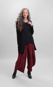 Front full body view of a woman wearing red alembika pants and the Alembika Pocket Top in black. This top has long sleeves and two front draped pockets that are longer than the front hem. 