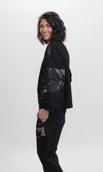 Load image into Gallery viewer, Left side top half view of a woman wearing the Alembika Bronze Top. This boxy top has long sleeves, a crew neck, and a mix of solid, velvet, printed, and quilted fabric. The top is black with bronze print
