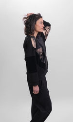 Load image into Gallery viewer, Right side top half view of a woman wearing the Alembika Bronze Top. This boxy top has long sleeves, a crew neck, and a mix of solid, velvet, printed, and quilted fabric. The top is black with bronze print.
