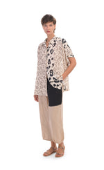 Load image into Gallery viewer, Front full body view of a woman wearing the alembika Cheetah Print Button Down Top. This top has different panels of black and taupe cheetah print on a creme background. The top has a button down front, short dolman sleeves, and a back pleat. on the bottom the woman is wearing cream pants with a black patch pocket.
