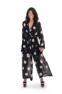 Front full body view of a woman wearing the alembika chiffon dot palazzo pant with a matching chiffon shirt. The pant and shirt is black with white dots. The fabric appears sheer. The pants are wide legged and end right above the ankles.