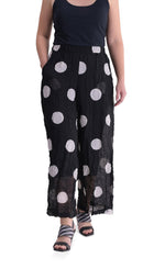 Load image into Gallery viewer, Front full body view of a woman wearing the alembika chiffon dot palazzo pant with a black tank. The pant is black with white dots. The fabric appears sheer. The pants are wide legged and end right above the ankles.
