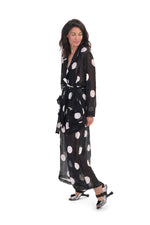 Load image into Gallery viewer, Left side full body view of a woman wearing the alembika chiffon dot palazzo pant with a matching chiffon shirt. The pant and shirt is black with white dots. The fabric appears sheer. The pants are wide legged and end right above the ankles.
