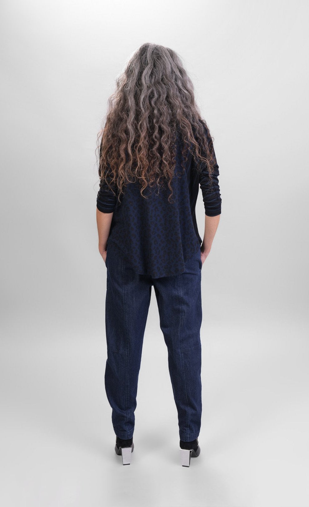 Back full body view of a woman wearing jeans and the alembika chiu raglan top. This top is navy with black and navy stripes on the shoulders and long sleeves and black animal print on the body.