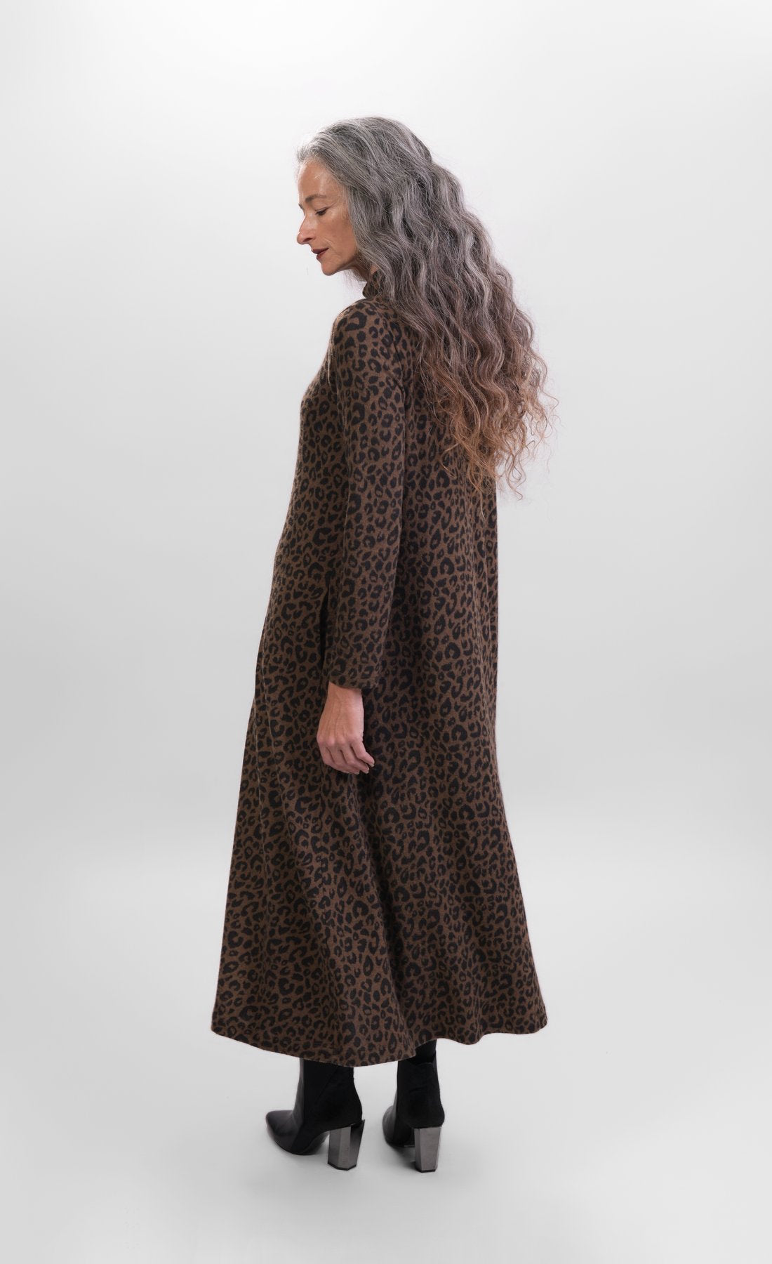 Back full body view of a woman wearing the alembika chiu swing dress. This dress is brown with black cheetah print. It has long sleeves and a turtleneck.