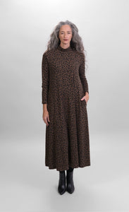 Front full body view of a woman wearing the alembika chiu swing dress. This dress is brown with black cheetah print. It has long sleeves, side pockets, and a turtleneck.
