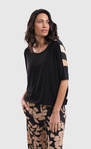 Front top half view of a woman wearing the alembika drapey dolman sunrise top. This top is black in the front and striped in the back with white and tan stripes. The top has elbow-length sleeves.
