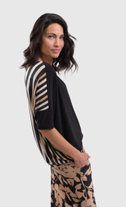 Right side top half view of a woman wearing the alembika drapey dolman sunrise top. This top is black in the front and striped in the back with white and tan stripes. The top has elbow-length sleeves.