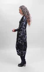 Load image into Gallery viewer, left side full body view of a woman wearing the alembika echo swing dress. This dress is grey, black, and blue tie dye with black dots all over it. It has a v-neck, a balloon skirt, and long sleeves.
