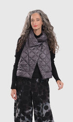 Load image into Gallery viewer, Front top half view of a woman wearing the alembika ether fina jacket vest in grey over a black long sleeve. This vest is a puffer vest. It features a large folded over collar and a single button closure towards the neck. 
