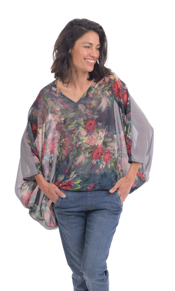 Front top half view of a woman wearing jeans and the alembika flora top. This top has a floral print on the front, an oversized fit, a v-neck, and 3/4 length sleeves.