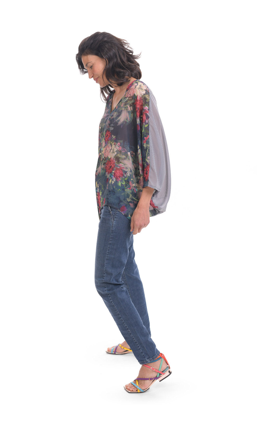 Left side full body view of a woman wearing jeans and the alembika flora top. This top has a floral print on the front, an oversized fit, a v-neck, and 3/4 length sleeves.