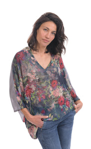 Front top half view of a woman wearing jeans and the alembika flora top. This top has a floral print on the front, an oversized fit, a v-neck, and 3/4 length sleeves.