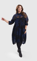 Load image into Gallery viewer, Front full body view of a woman wearing the alembika floral check wonderful dress. This long sleeved dress is black mesh/sheer with blue and black houndstooth/floral printed pieces of fabric all over it. The front of the dress has a 3/4 button up and a draped pocket on the left side. 

