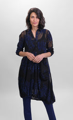 Load image into Gallery viewer, Front full body view of a woman wearing the alembika floral check wonderful dress. This long sleeved dress is black mesh/sheer with blue and black houndstooth/floral printed pieces of fabric all over it. The front of the dress has a 3/4 button up and a draped pocket on the left side. 
