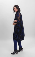 Load image into Gallery viewer, Left side full body view of a woman wearing the alembika floral check wonderful dress. This long sleeved dress is black mesh/sheer with blue and black houndstooth/floral printed pieces of fabric all over it. 
